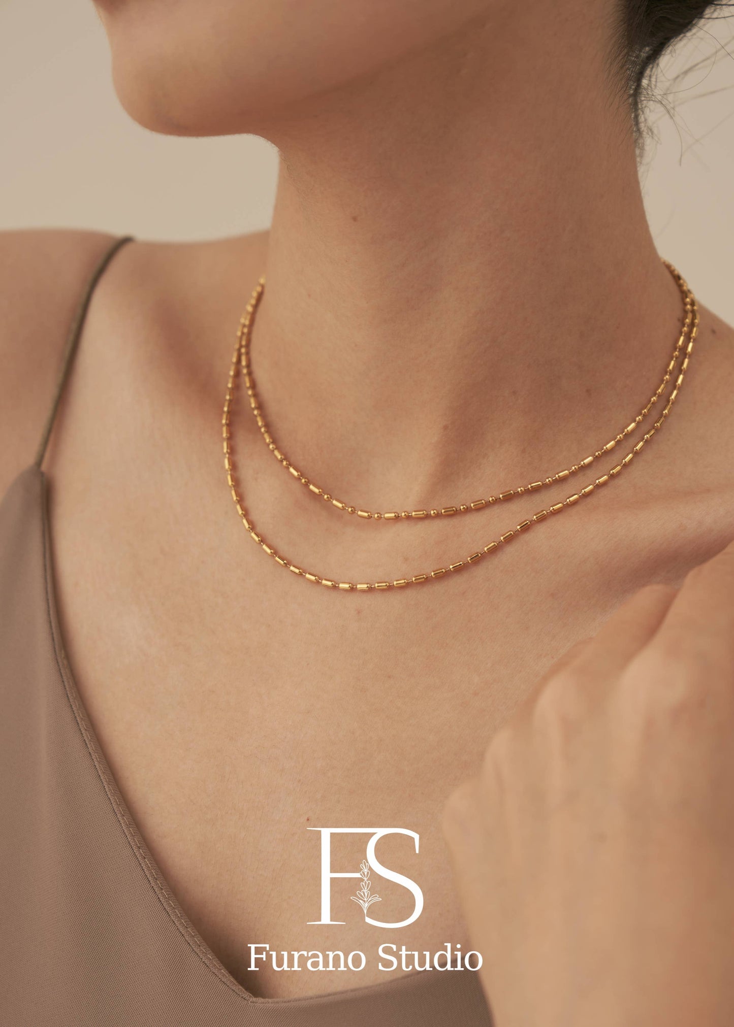 Gold necklace on a person with 'Furano Studio' logo