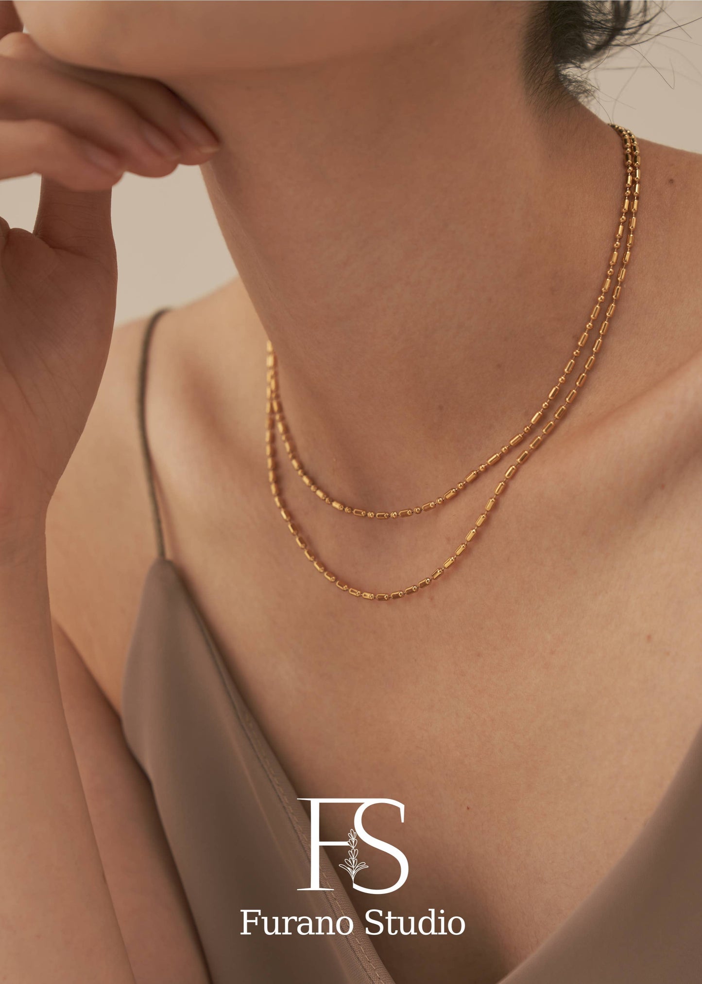 Gold necklace on a person with Furano Studio logo