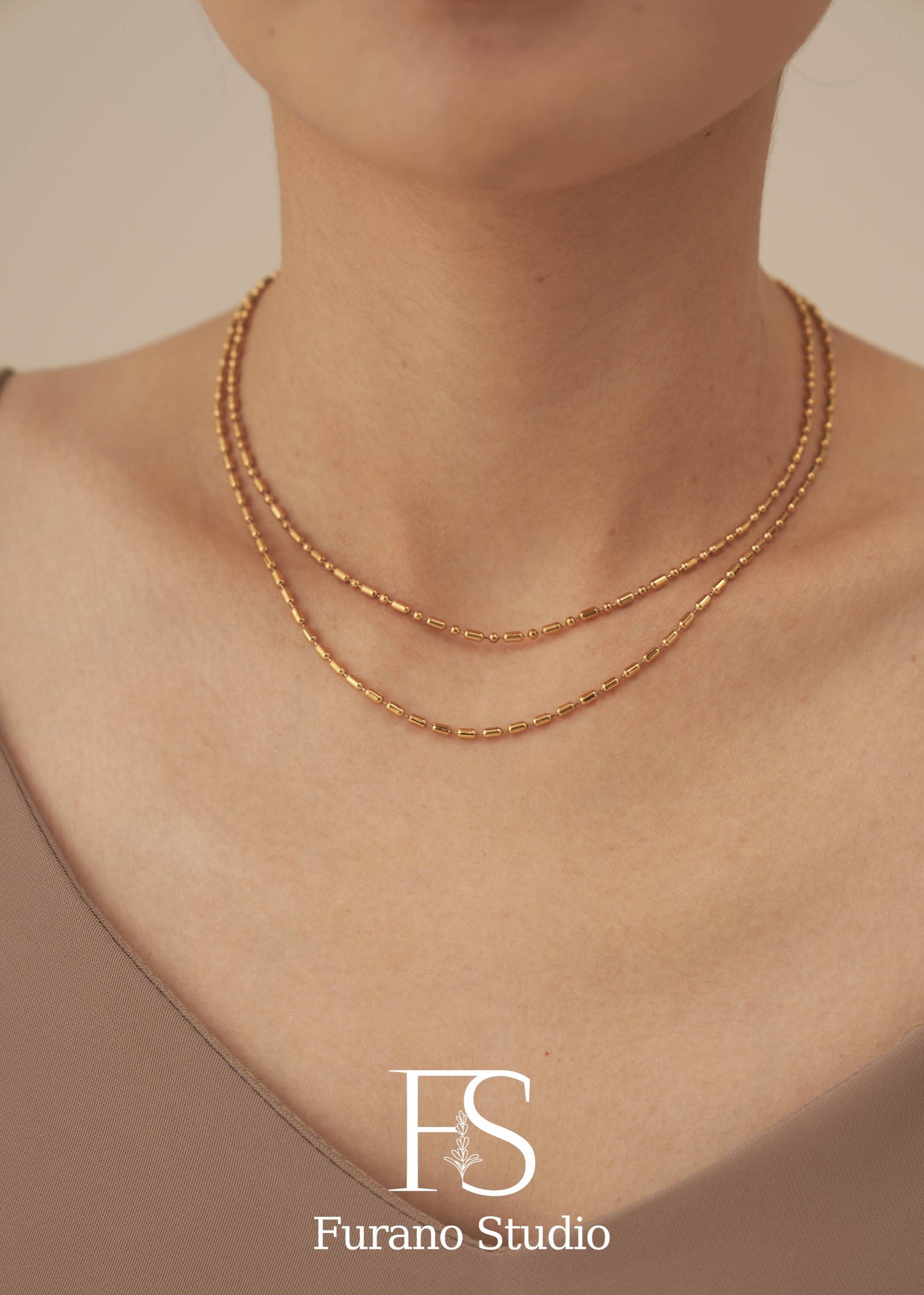 Gold necklace on a person's neck with 'Furano Studio' logo.