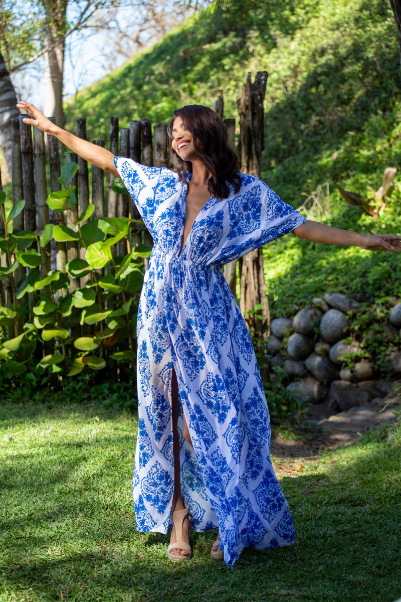 Woman in a blue and white patterned dress standing outdoors with arms outstretched.