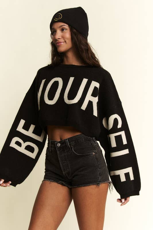 Person wearing a black sweater with 'BE YOURSELF' text on a beige background