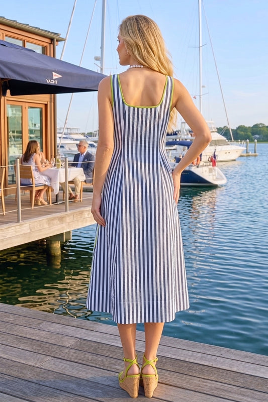 Woman in a striped dress standing on a dock by the water with yachts in the background.