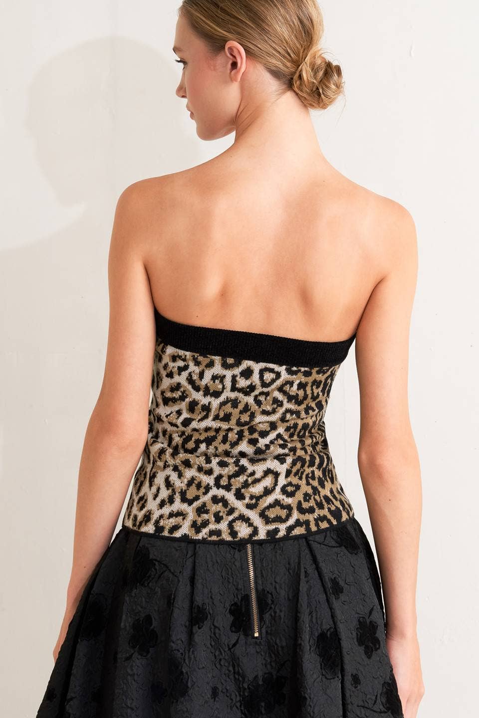Woman wearing a strapless dress with leopard print top and black skirt on a plain background