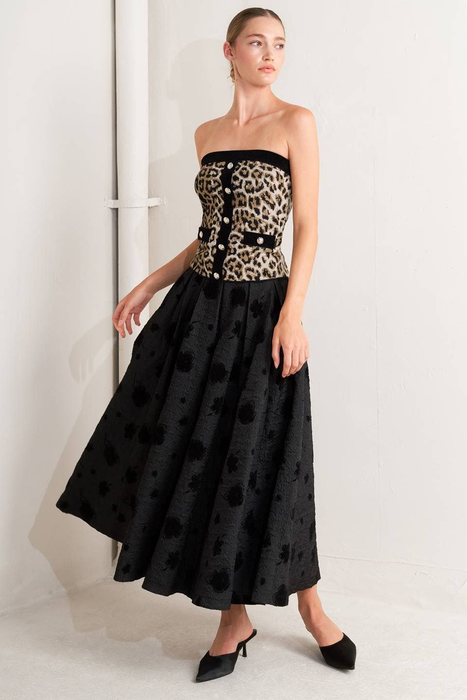 Woman wearing a black strapless dress with leopard print bodice against a white background