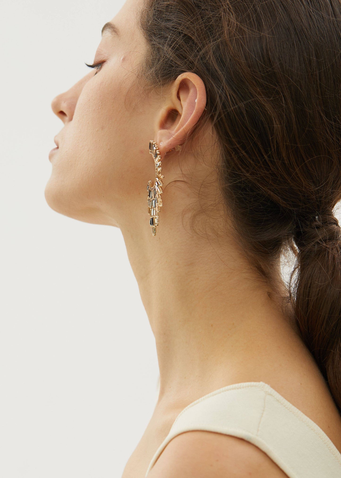 Close-up of a woman wearing a gold earring on a plain background