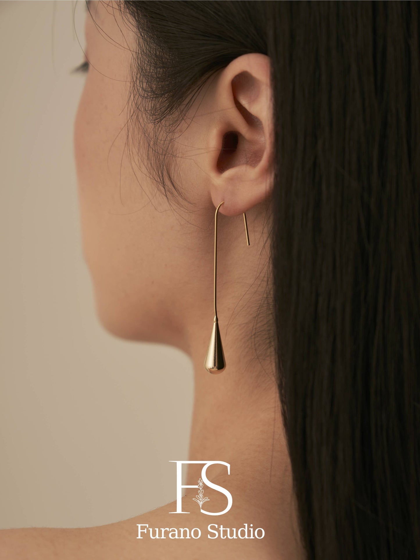 Gold earring worn by a person with a neutral background, featuring Furano Studio logo.