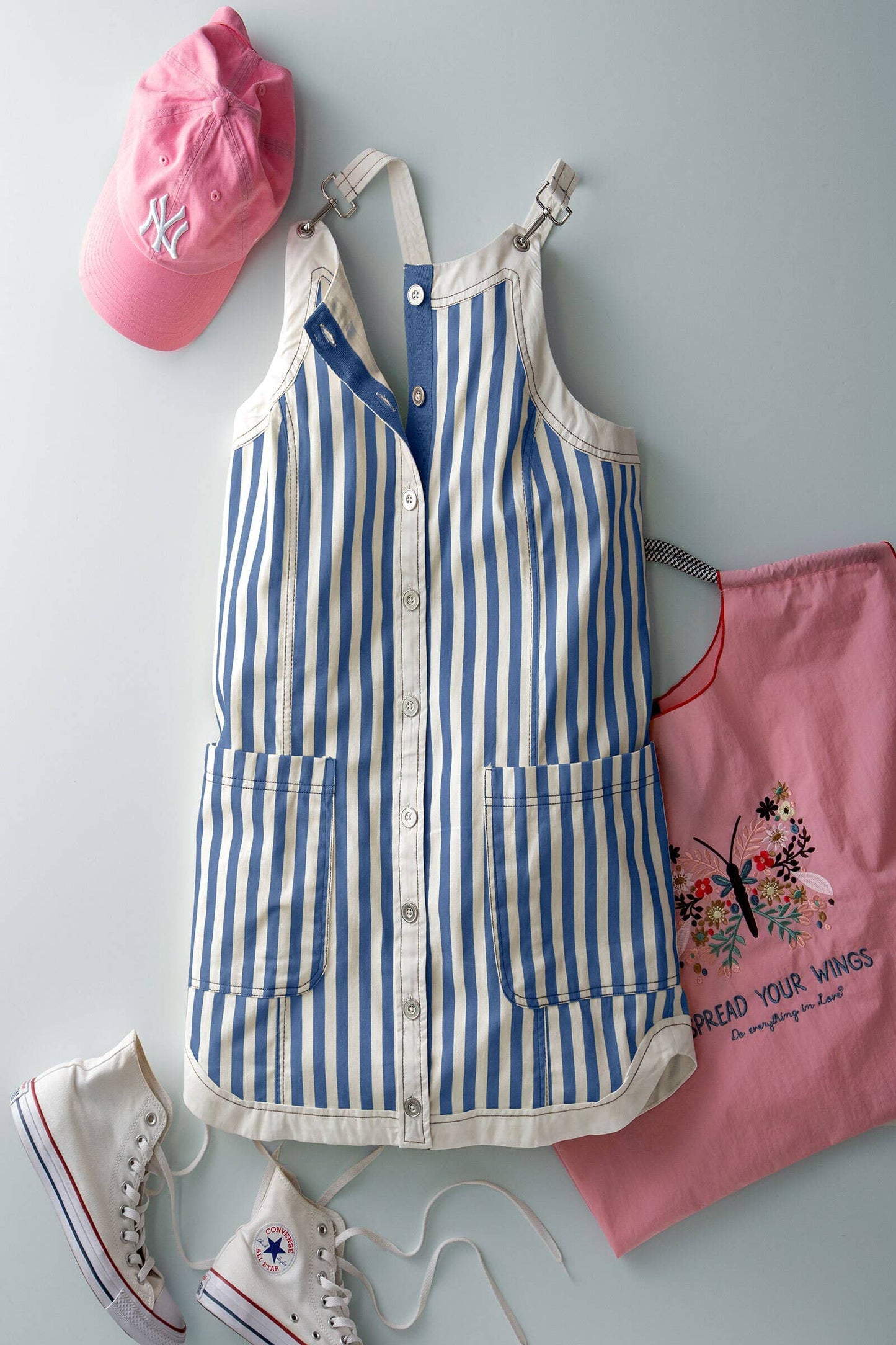 Blue and white striped apron with pink cap, pink bag, and white sneakers on a light gray background