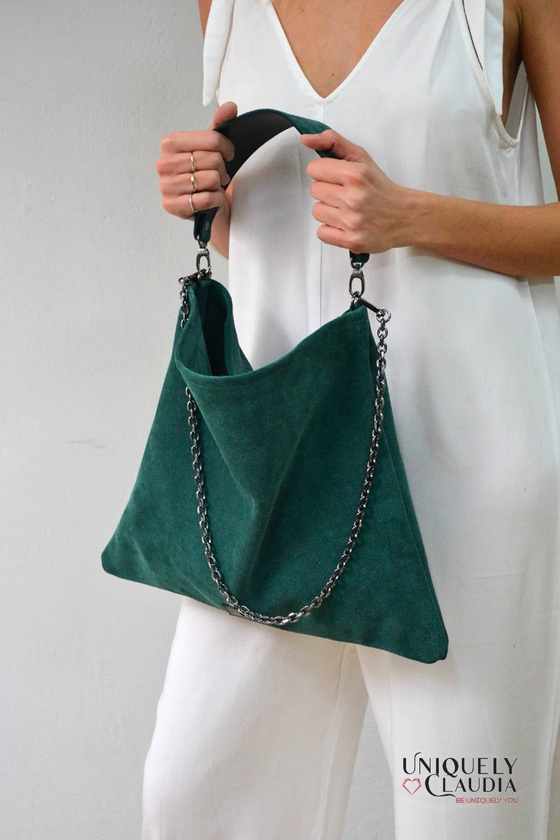 Green handbag with chain detail held by a person wearing a white outfit, against a plain background.