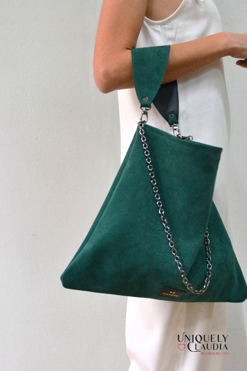 Green handbag with chain detail held by a person against a plain background