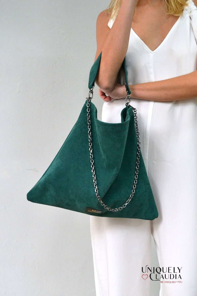 Green handbag with chain detail held by a person wearing a white dress on a light gray background.