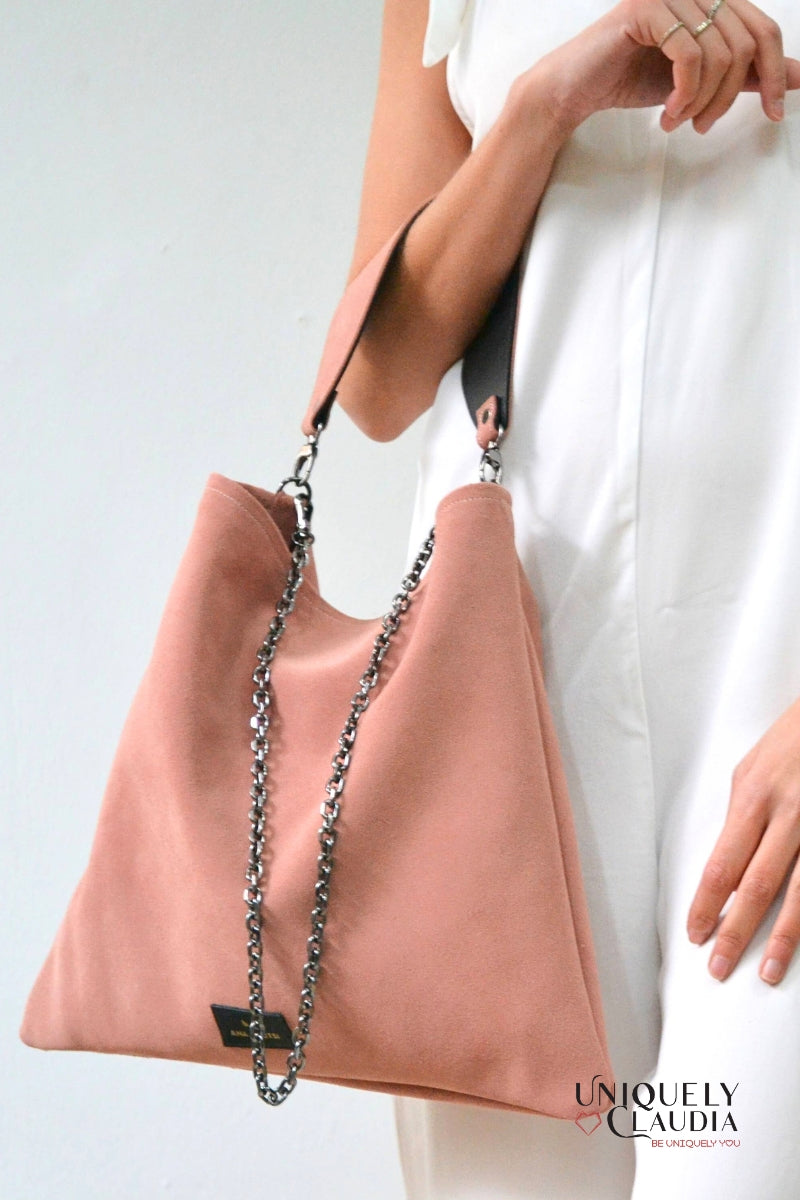 Pink handbag with a chain detail held by a person wearing white pants on a light gray background.