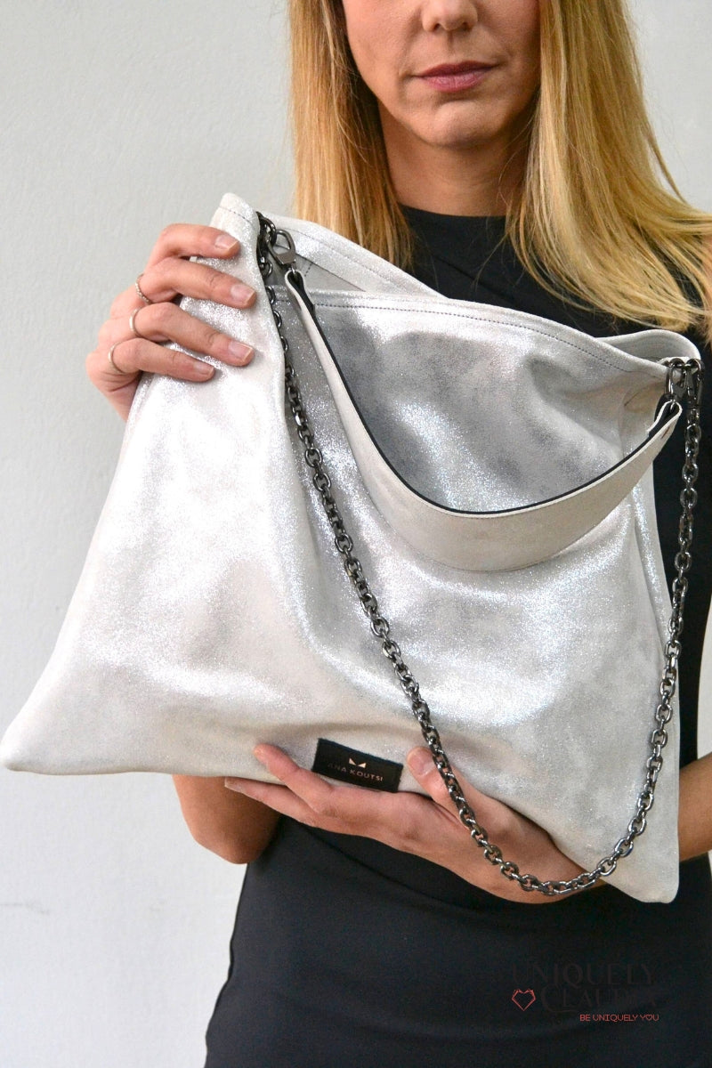 Person holding a silver handbag with a chain detail against a plain background