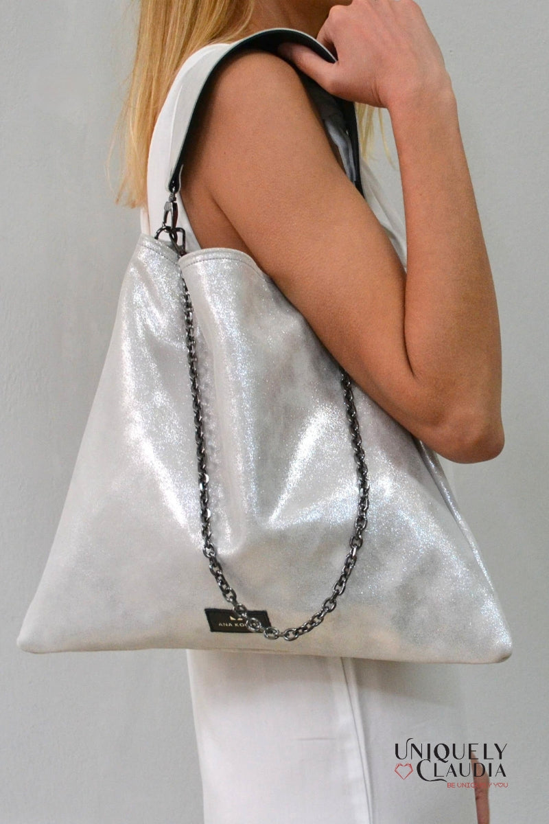 Person holding a silver metallic handbag with a chain detail on a plain background