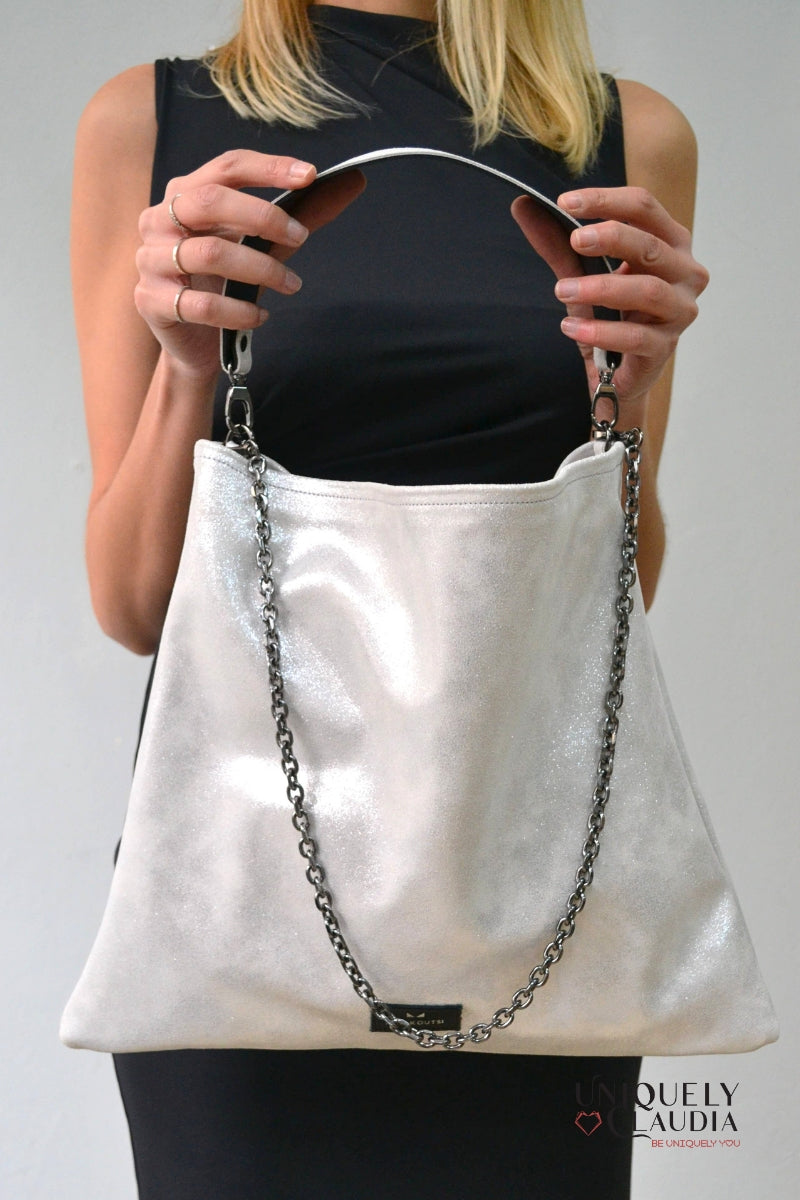 Person holding a silver handbag with a chain detail against a plain background