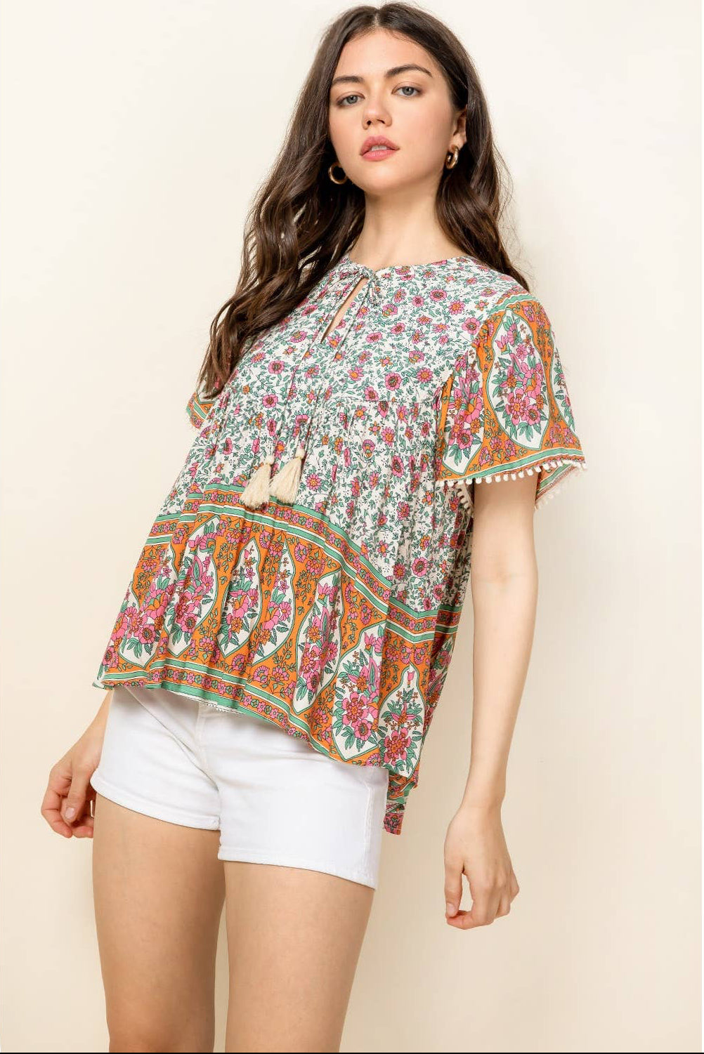 Woman wearing a floral blouse and white shorts on a beige background