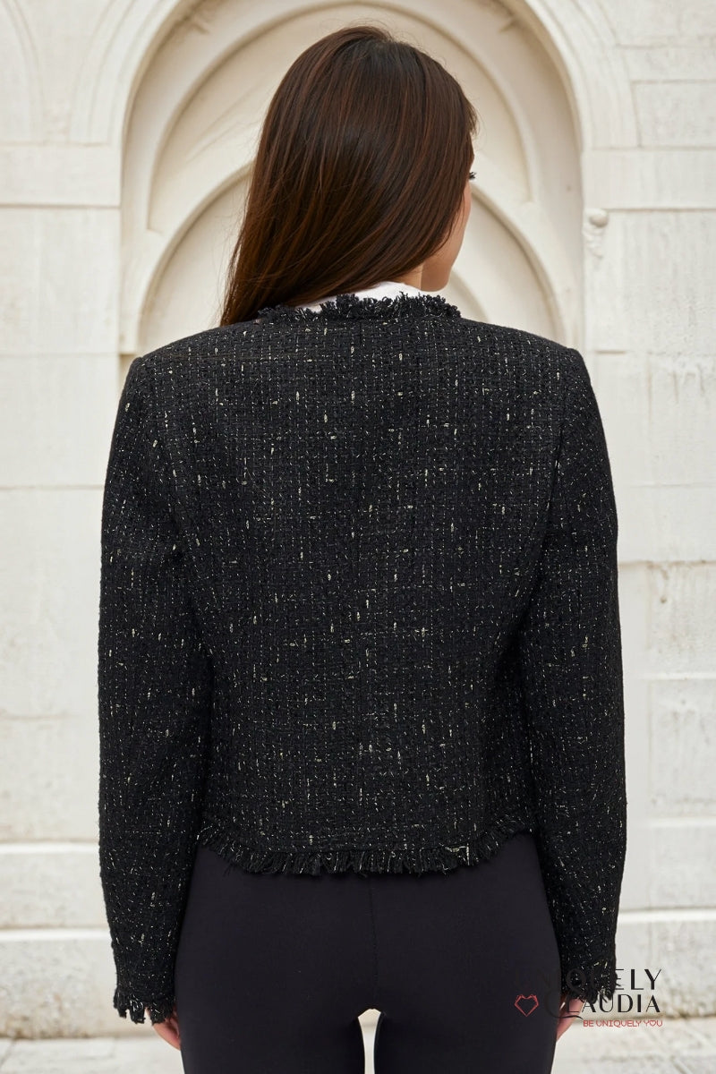 Person wearing a black textured jacket standing against a light-colored wall.