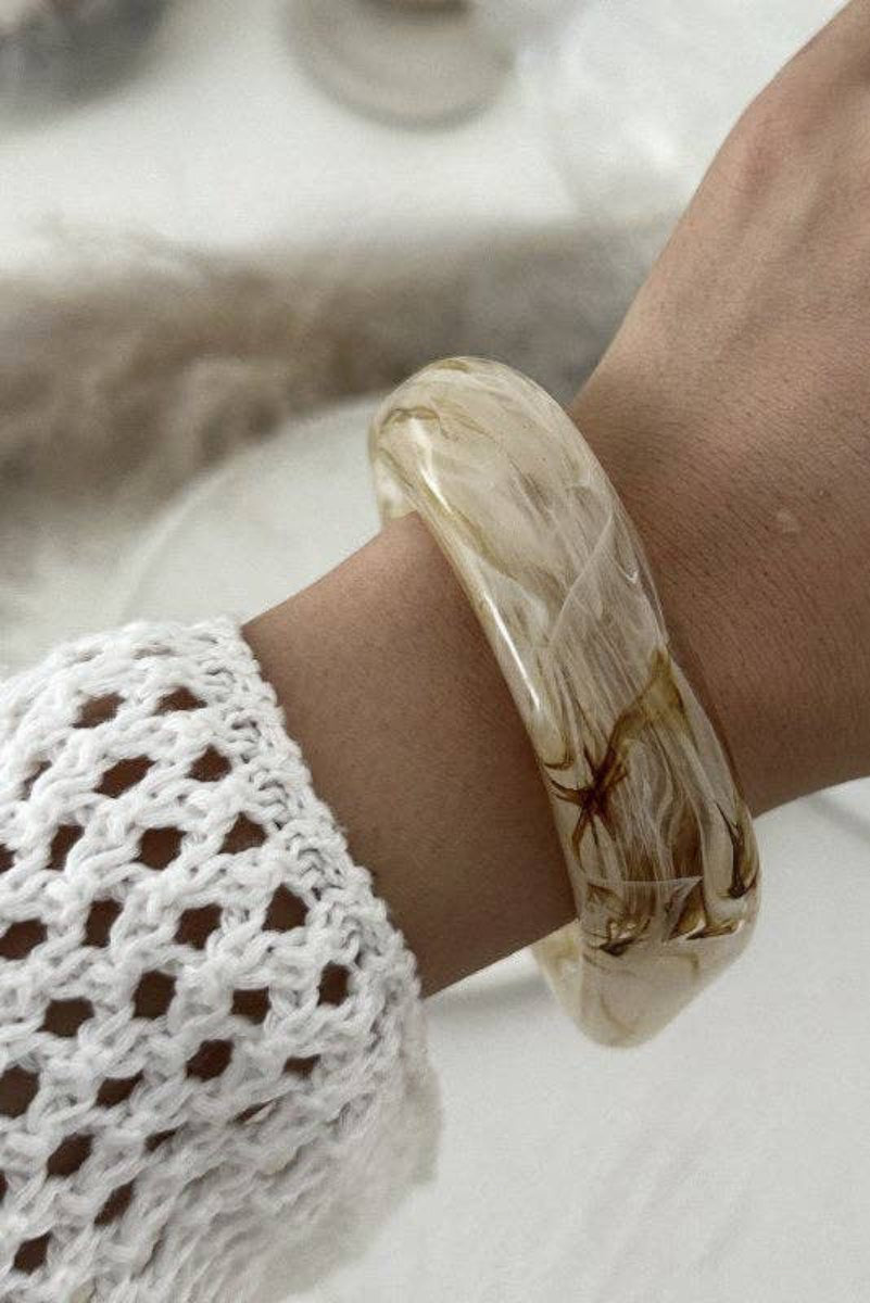 Hand wearing a marbled beige bracelet on a blurred background