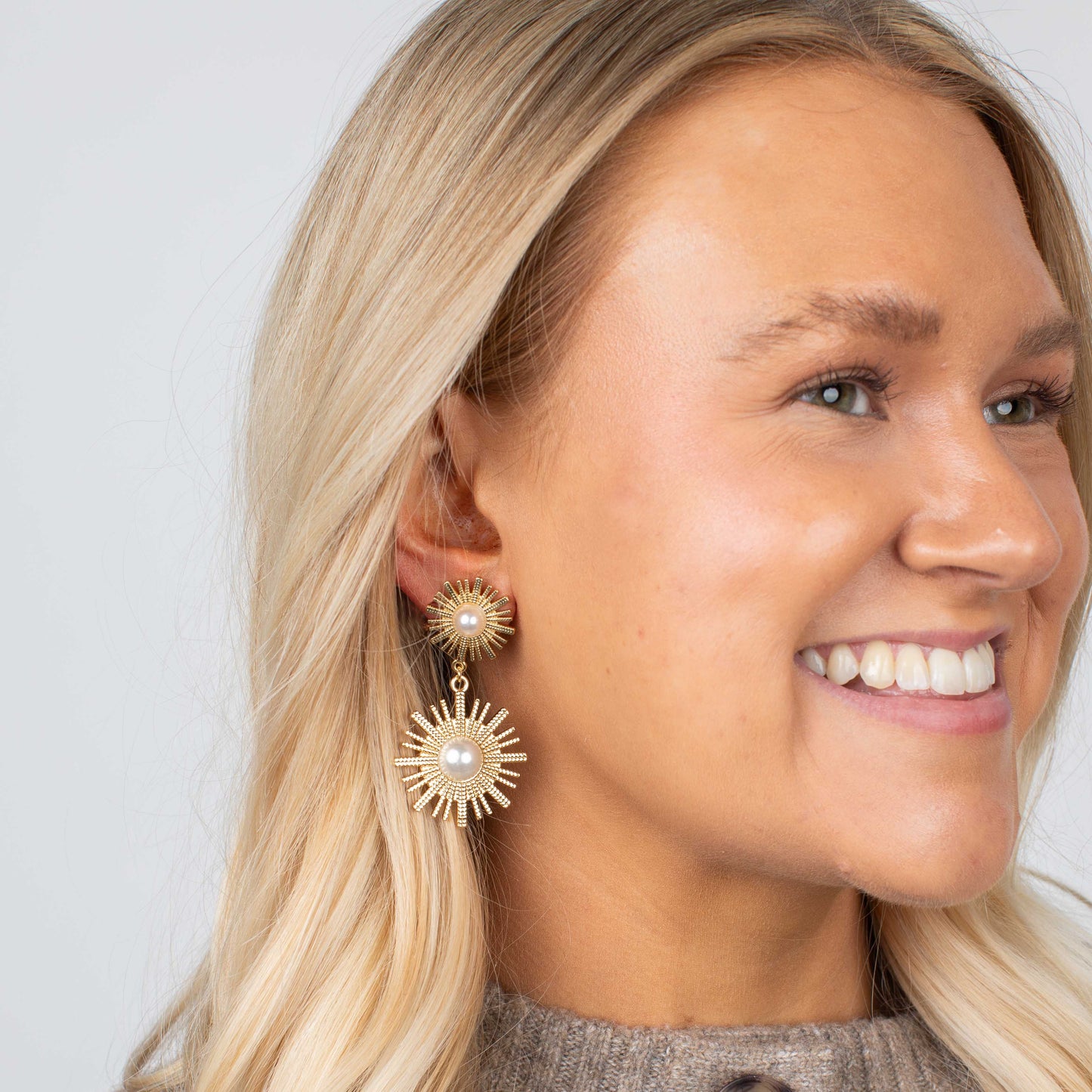 Woman wearing gold earrings with a pearl center against a plain background