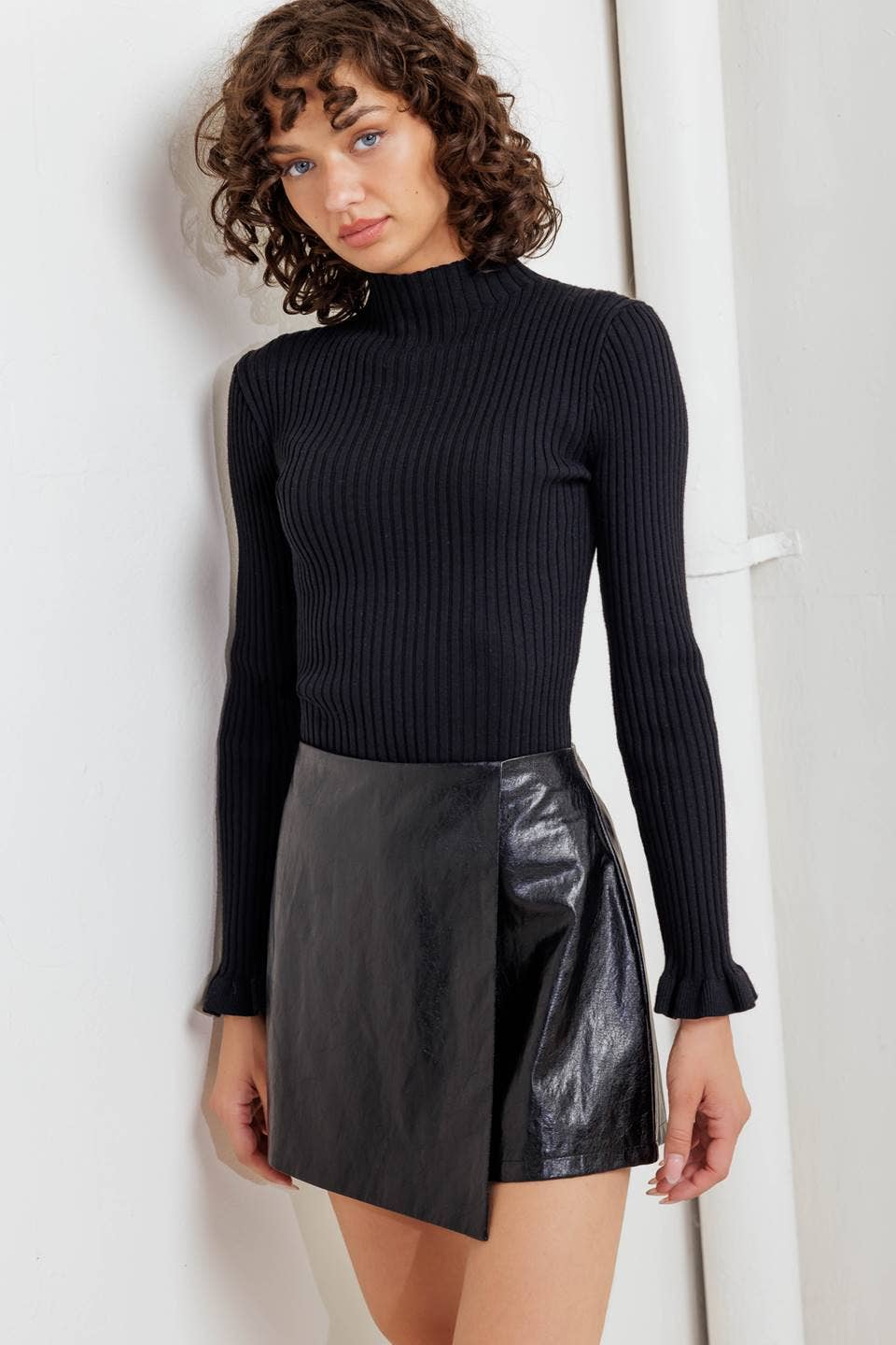 Woman wearing a black ribbed sweater and black leather skirt against a white background