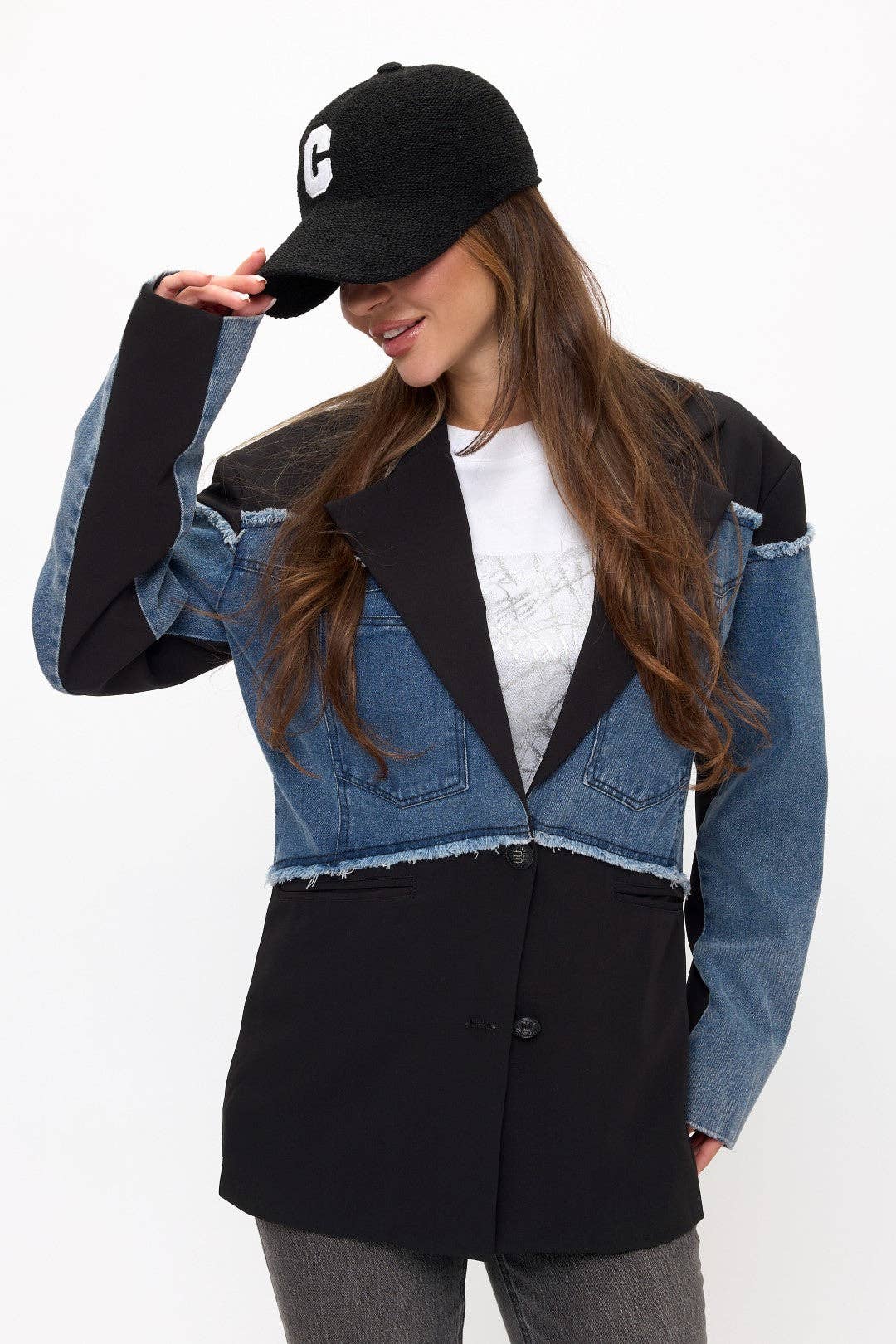 Woman wearing a black and denim jacket with a white shirt underneath, on a plain background