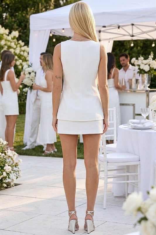Woman in a white dress standing outdoors at a formal event with floral decorations and tables.