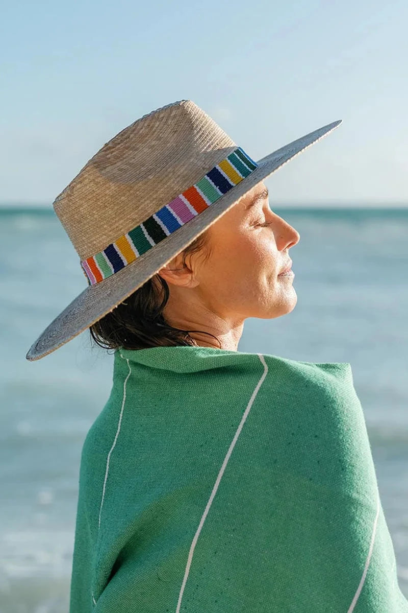 Person wearing a colorful striped hat and green blanket by the ocean