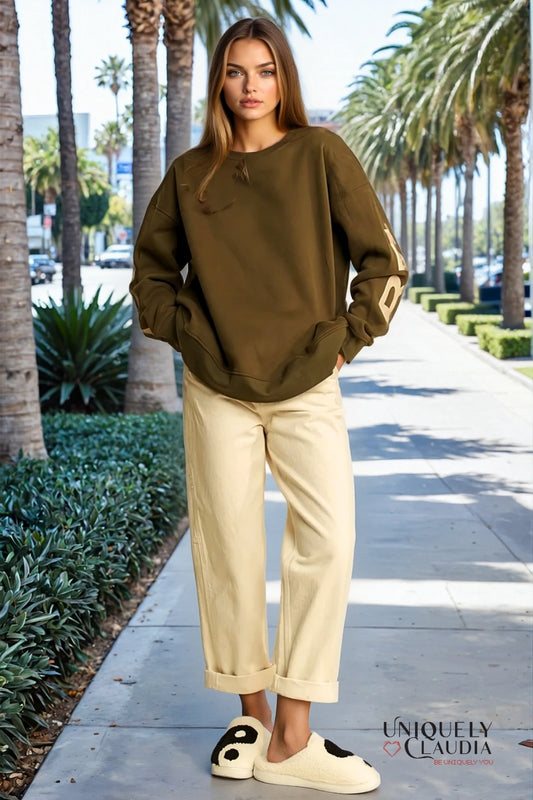 Woman wearing a green sweatshirt and beige pants on a palm tree-lined street.