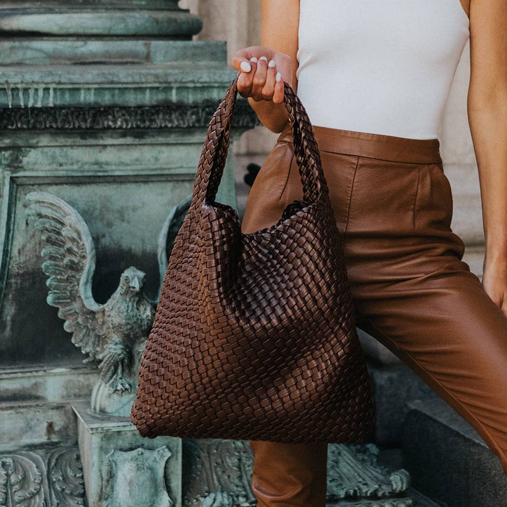 Person holding a woven brown handbag with a classical sculpture in the background