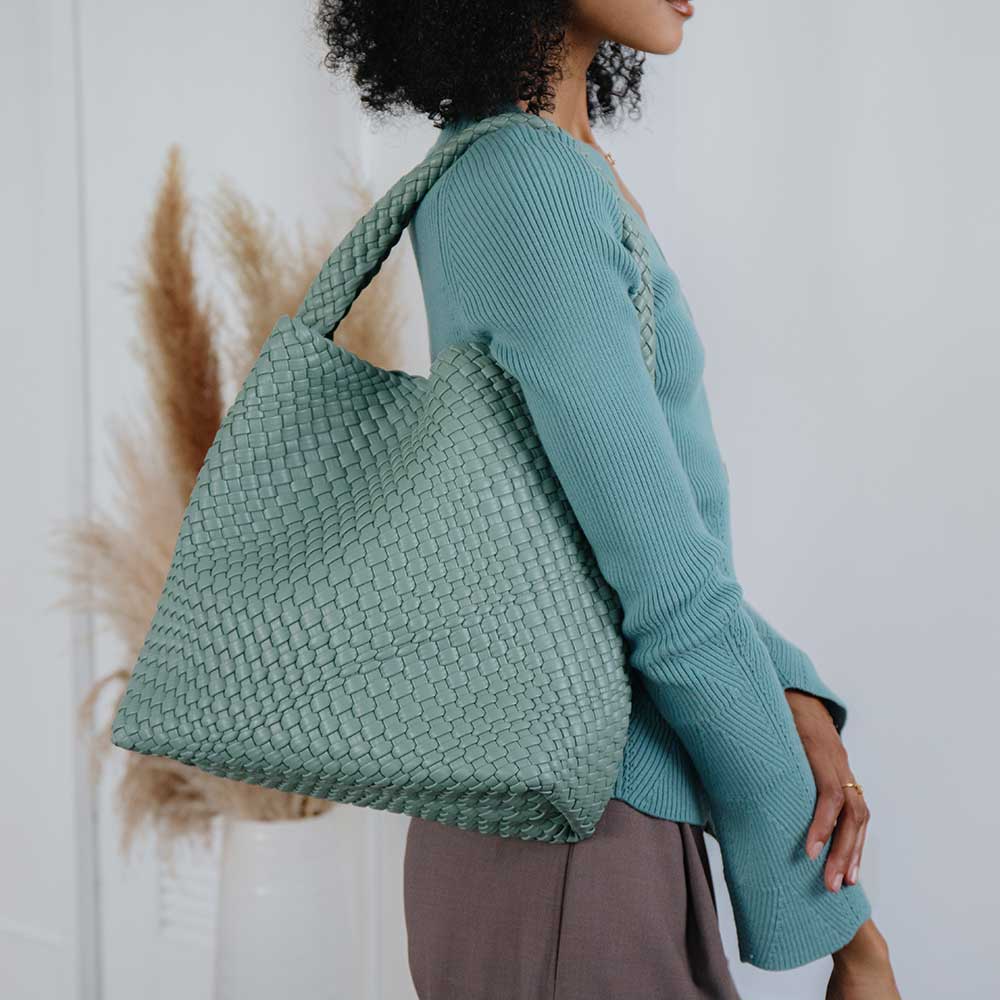 Woman wearing a teal woven bag against a neutral background
