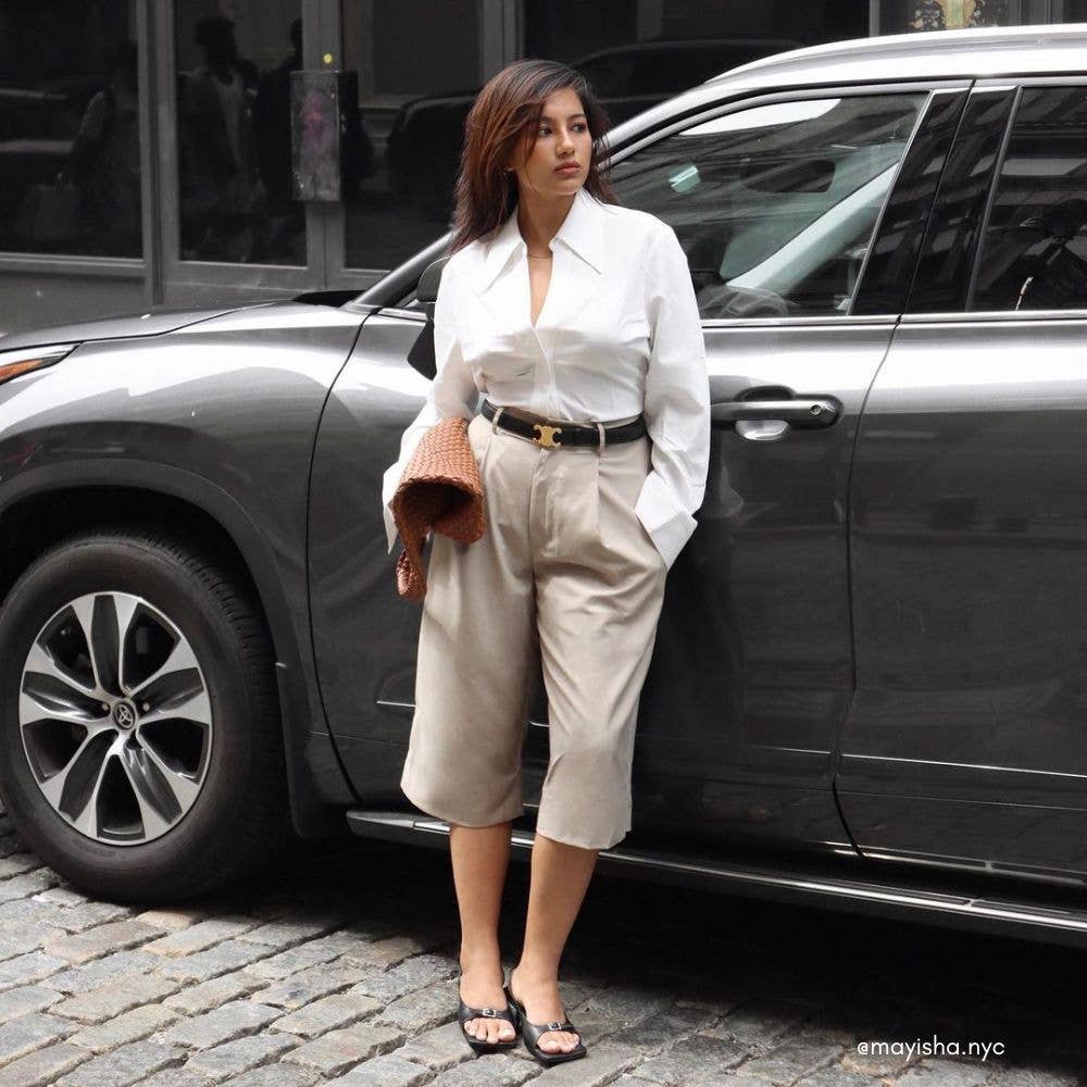 Woman in a white shirt and beige pants standing next to a car