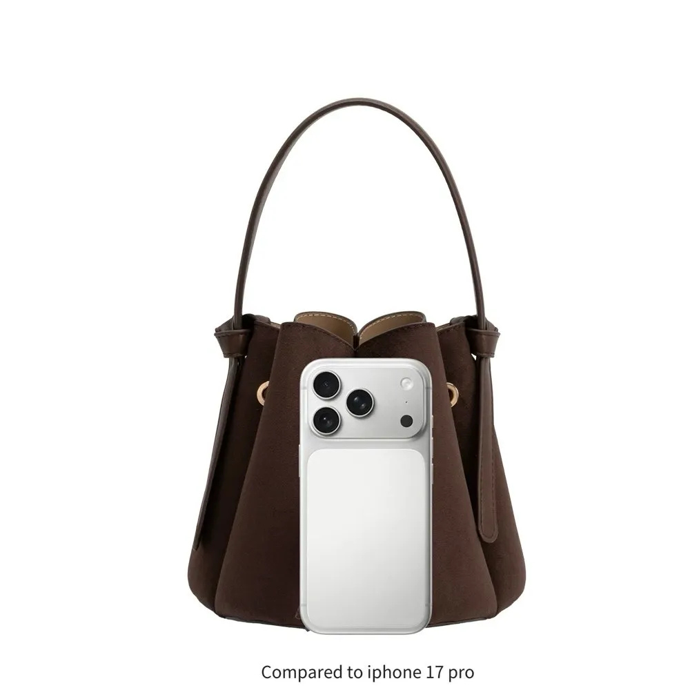 A dark brown bucket-style handbag with a single shoulder strap, shown against a plain white background. A silver smartphone is placed in front of the bag for scale, with text below reading 'Compared to iphone 17 pro'.