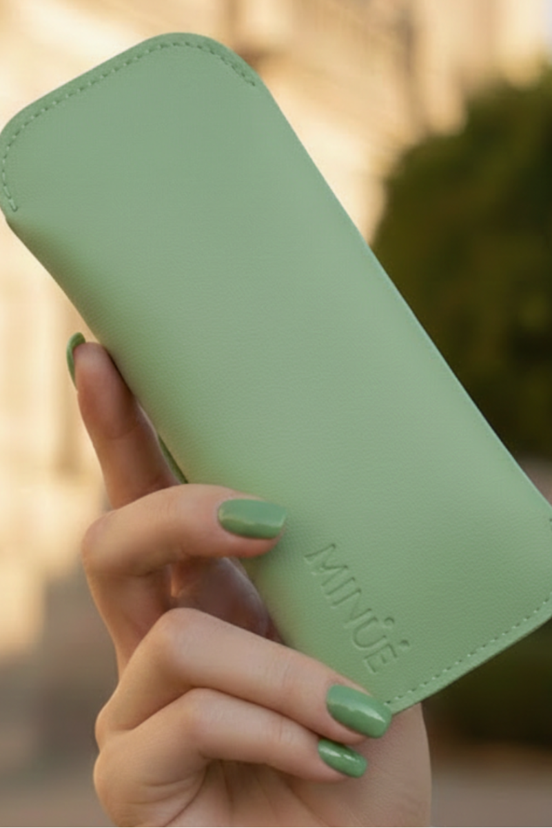 Hand holding a green phone case with 'MINUE' branding outdoors.