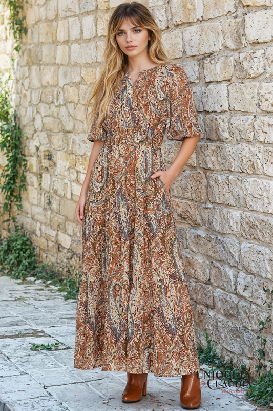 Woman in a patterned dress standing against a stone wall.