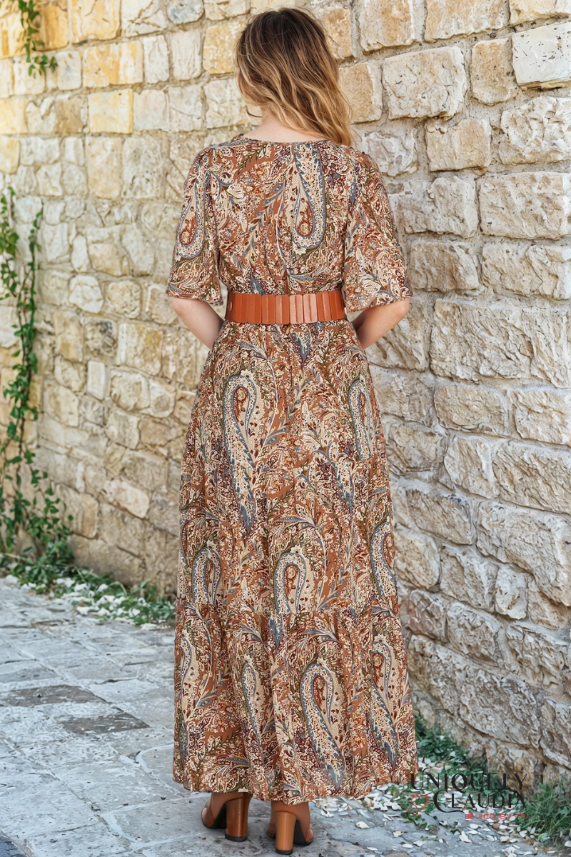 Woman wearing a patterned dress standing against a stone wall.