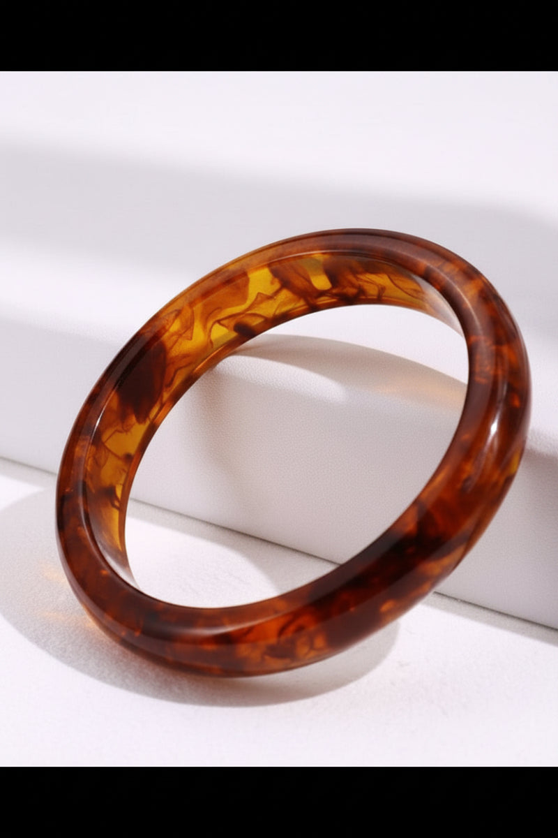 Tortoiseshell bangle on a white surface with green leaves in the background