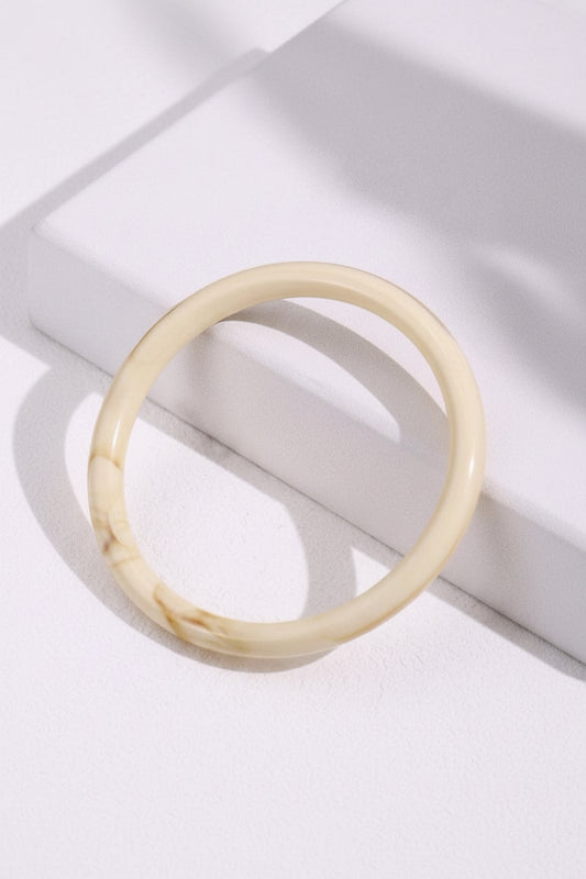 Beige bracelet on a white surface with green leaves