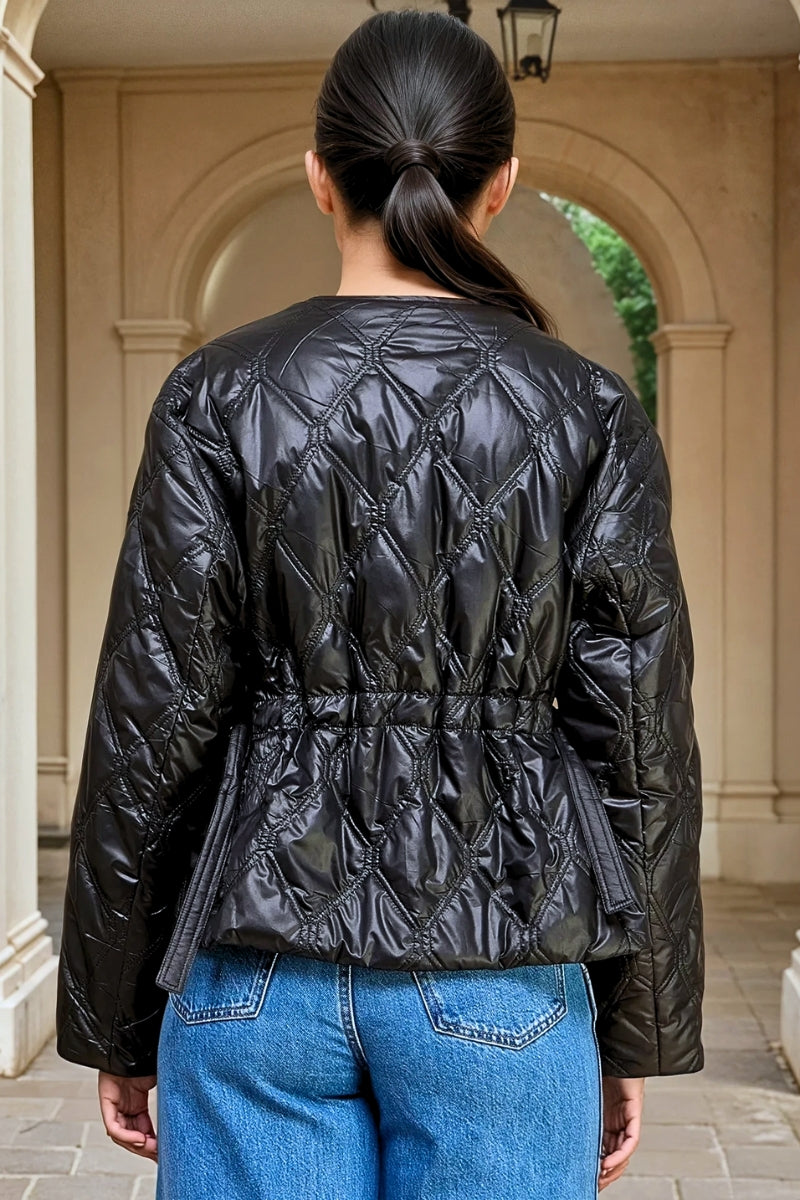 Person wearing a black quilted jacket with blue jeans standing in an outdoor setting.
