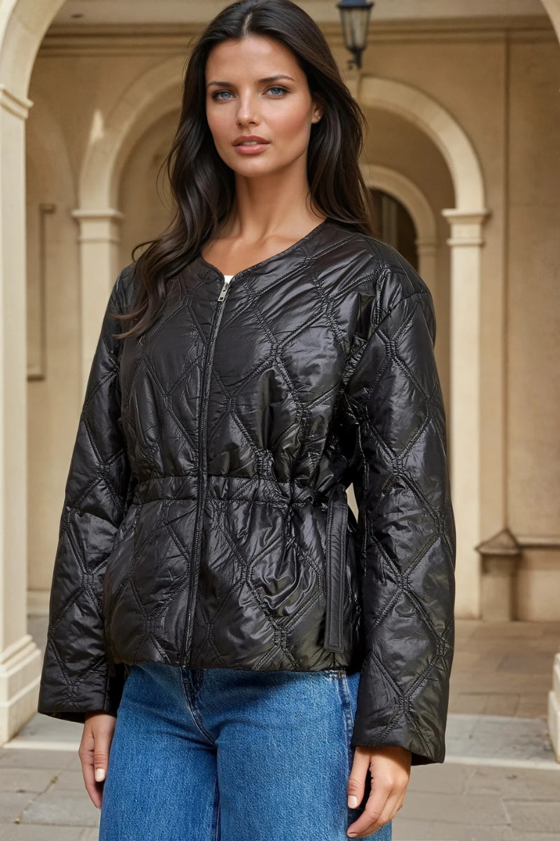 Woman wearing a black quilted jacket and blue jeans standing in front of architectural columns.