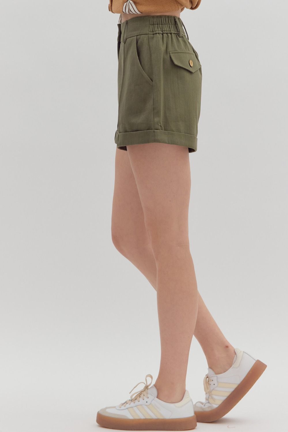 Person wearing olive green shorts and white sneakers on a plain background