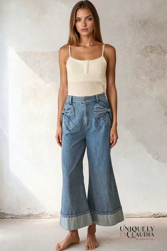 Woman wearing a beige top and blue jeans against a textured wall.