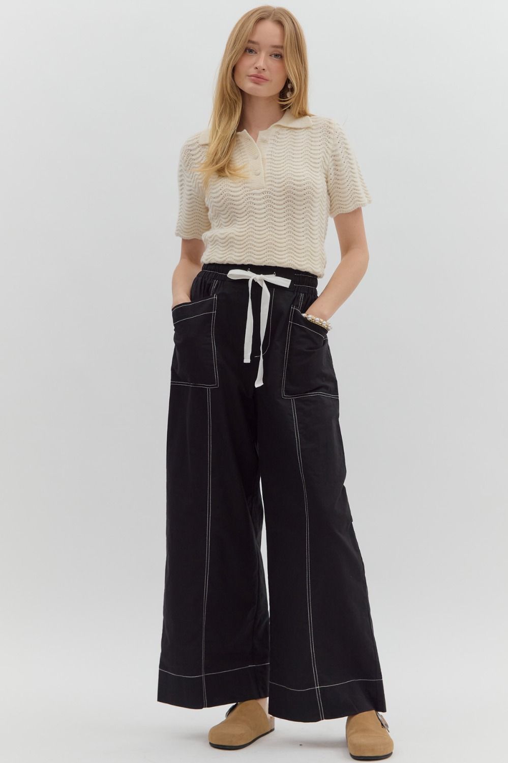 Woman wearing a cream knit top and black wide-leg pants on a white background