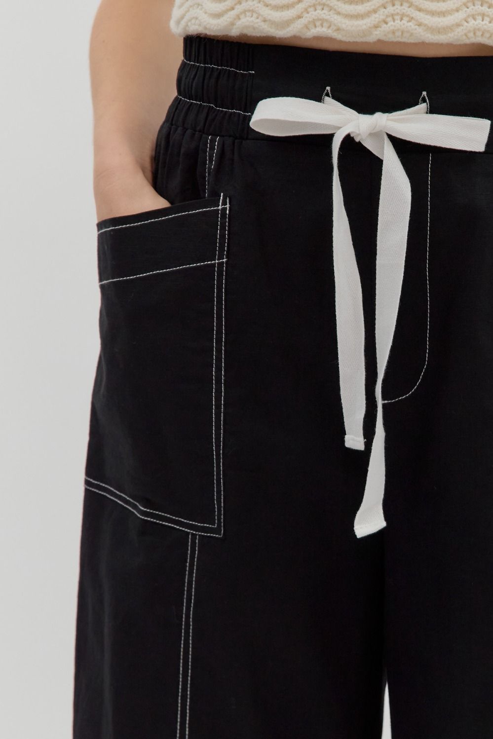 Black pants with white stitching and a white tie on a plain background