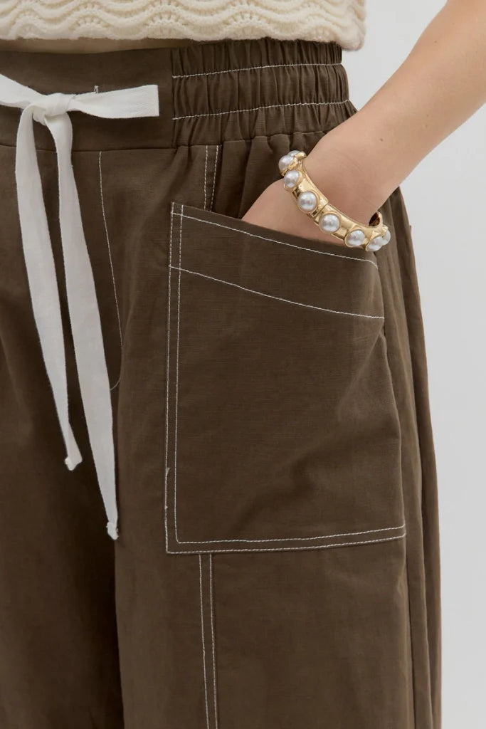 Brown pants with a white drawstring and pearl bracelet on a plain background