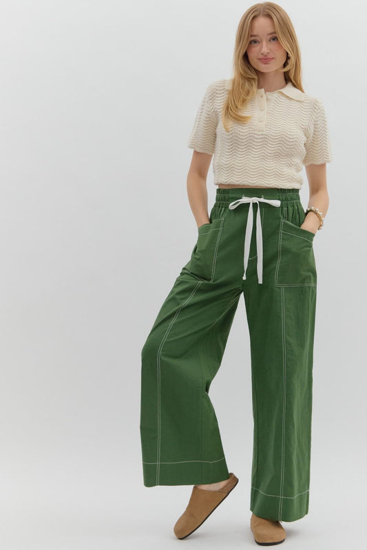 Woman wearing a cream top and green pants with a white background