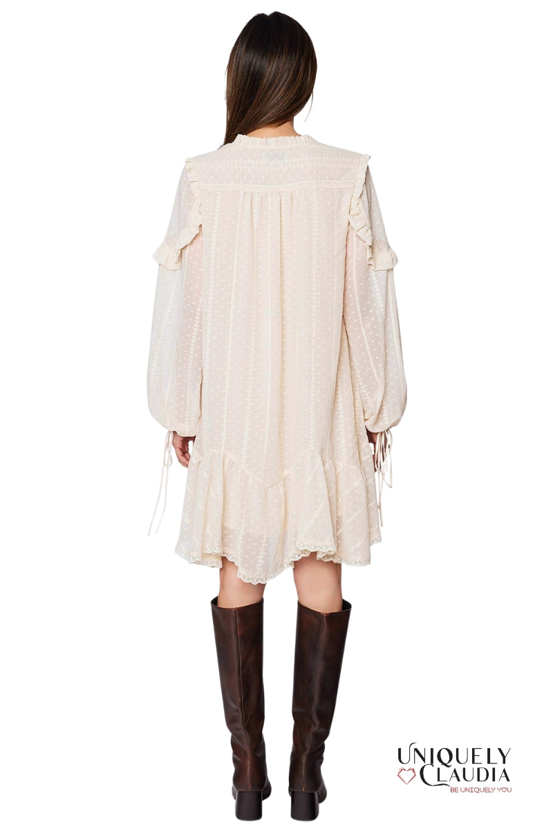 Woman wearing a cream-colored dress with long sleeves and brown knee-high boots on a white background.