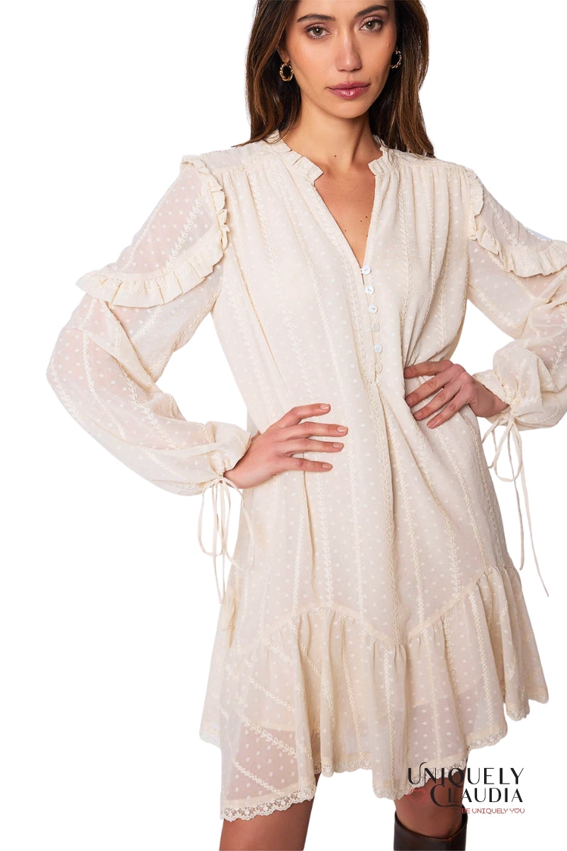 Woman wearing a white dress with long sleeves and ruffled details on a white background.