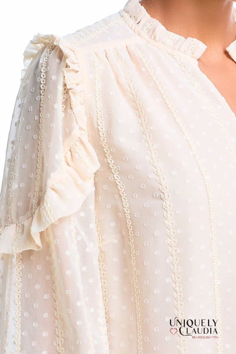 Close-up of a white blouse with ruffled sleeves and lace details, featuring the brand 'Uniquely Claudia'.
