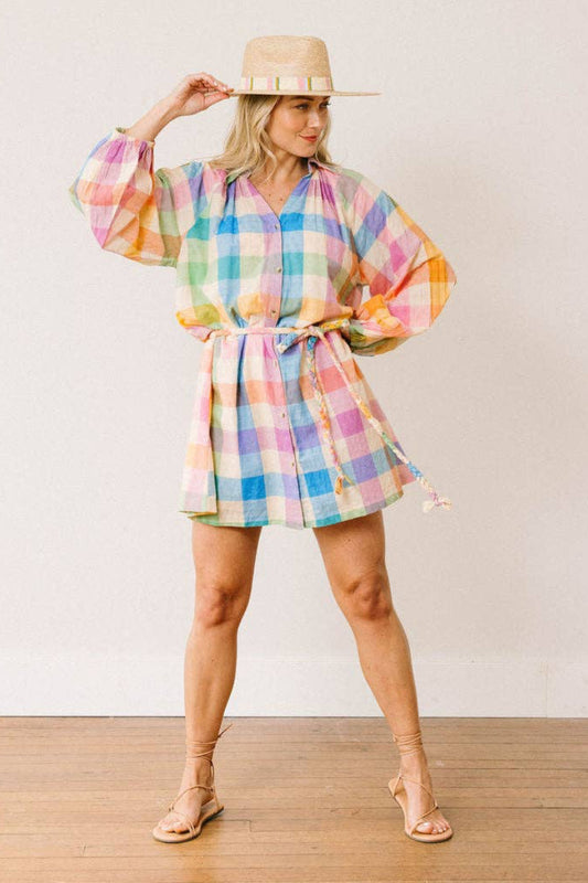 Woman wearing a colorful checkered dress and straw hat on a plain background