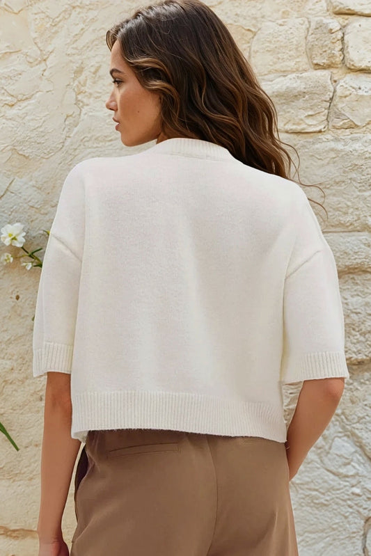 Woman wearing a white sweater and beige pants against a stone wall, with 'Uniquely Claudia' branding.