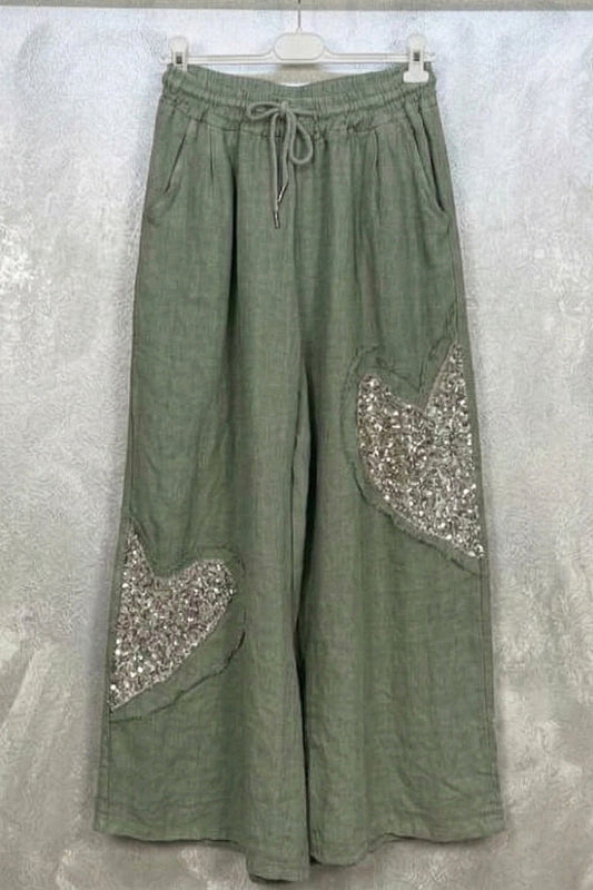 Green wide-leg pants with sequin patches on a hanger against a light gray background